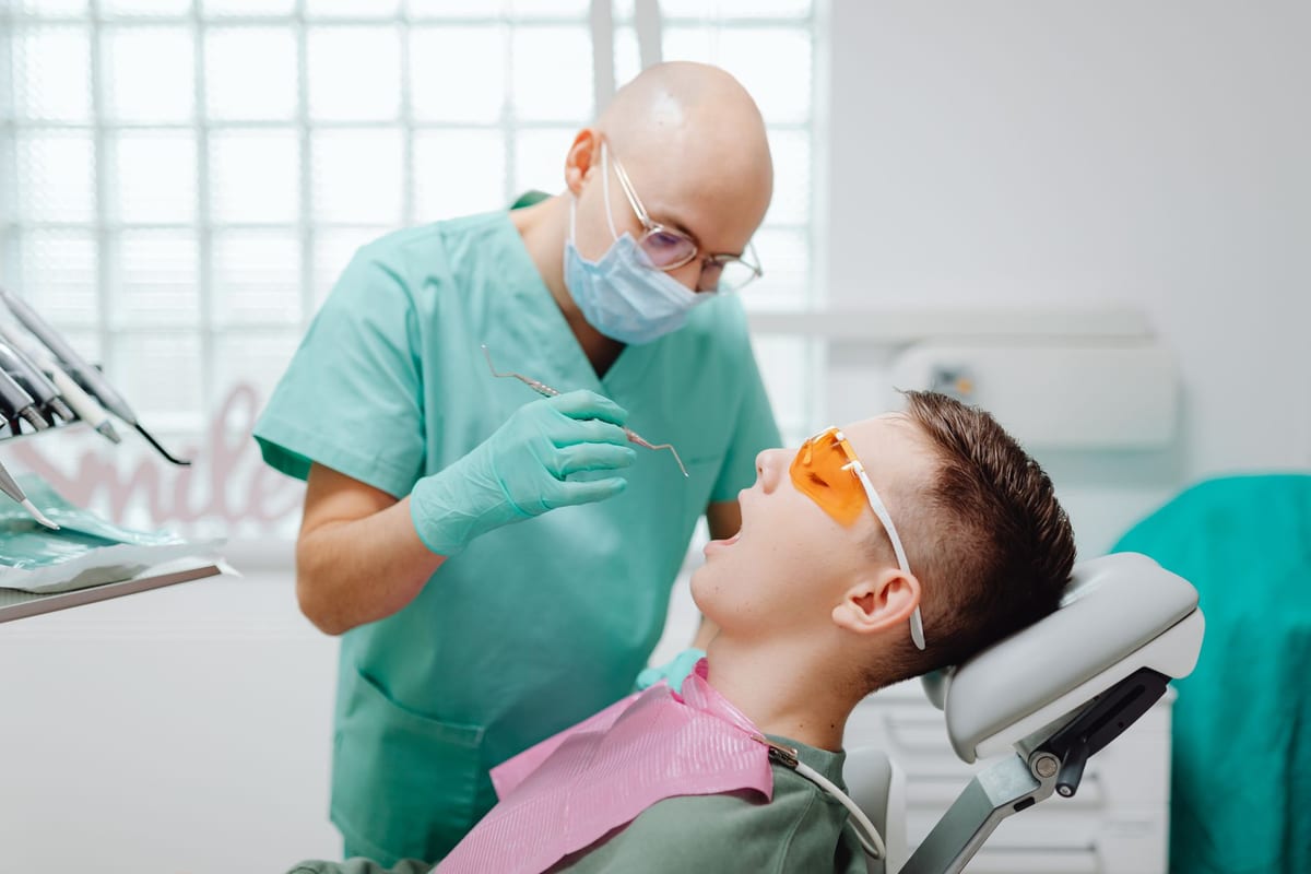 A masked dentist examining a reclined patient with a probe and mirror