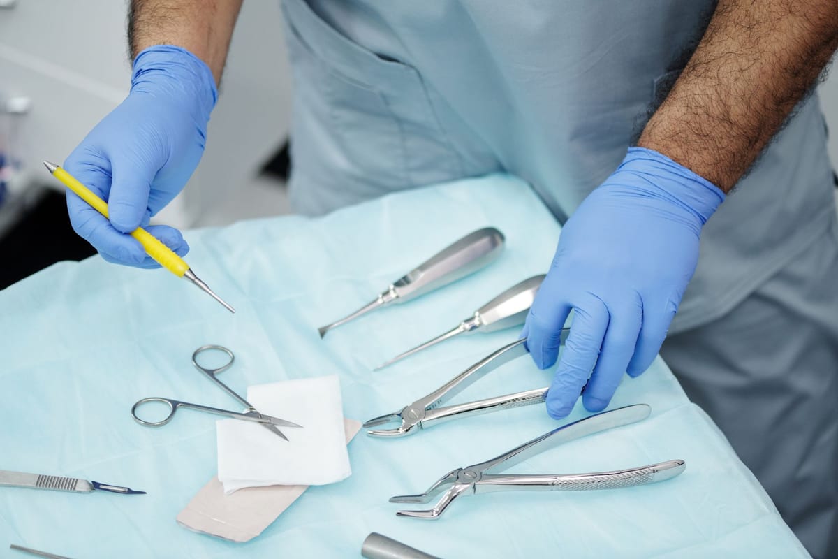 Gloved hands laying out extraction forceps and elevators on a blue drape